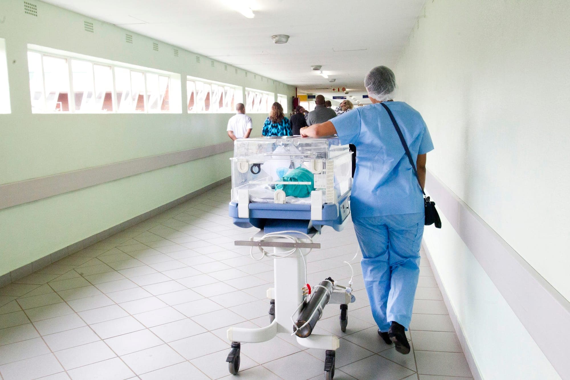 A healthcare worker moving neonatal equipment through a South African hospital corridor