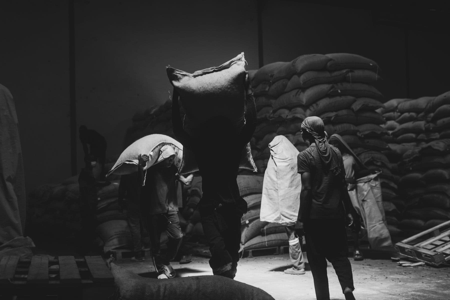 Workers move large sacks through a warehouse.